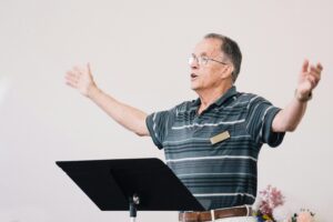 Senior man conducting choir passionately indoors. Elder leadership and expressive singing.