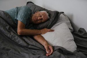 Elderly man resting comfortably in bed, serene indoor atmosphere.